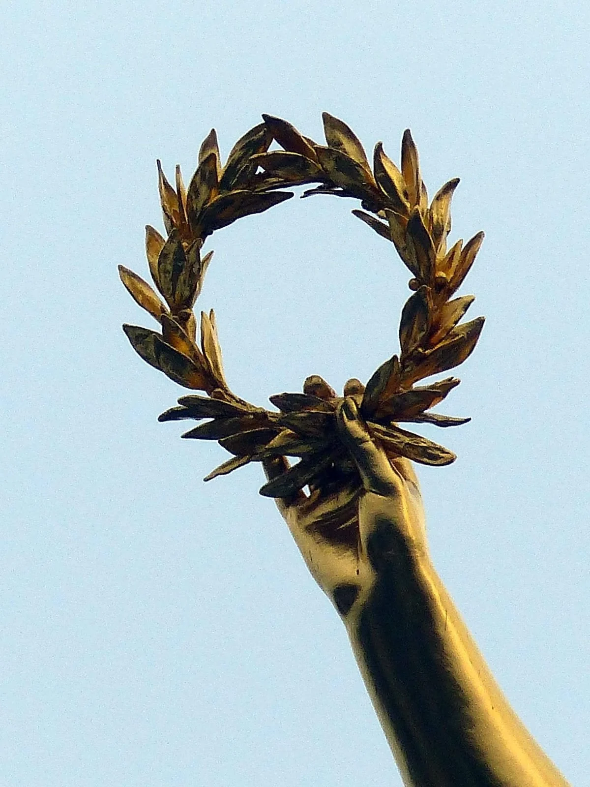 Mano dorada sosteniendo una corona de laurel contra el cielo